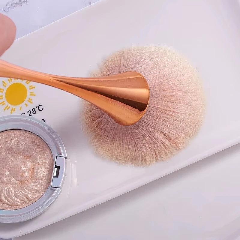 Rose gold fan brush with soft bristles, ideal for applying powder, highlighter, blush, and finishing touches